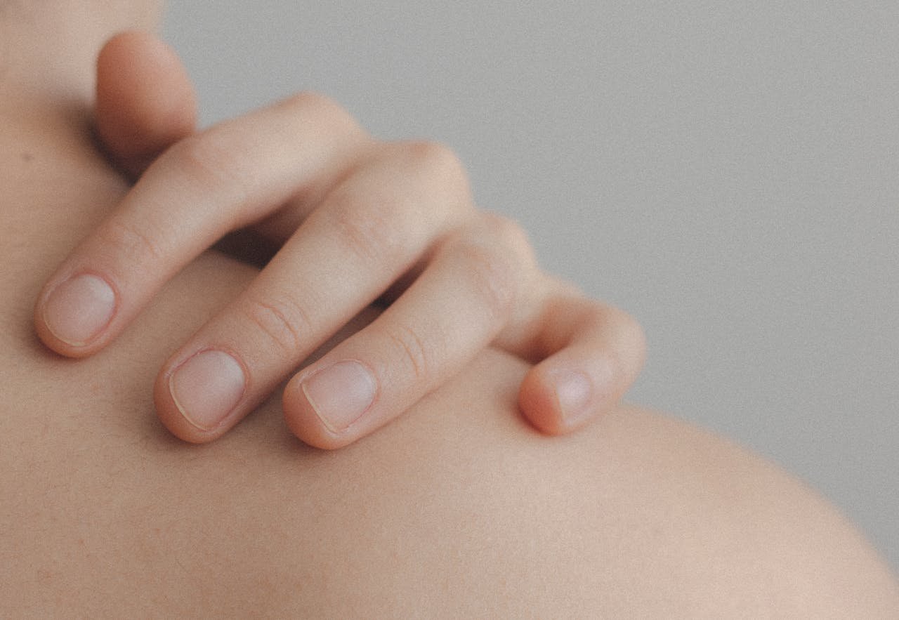 A gentle close-up of a hand resting on a person's shoulder, emphasizing skin texture.